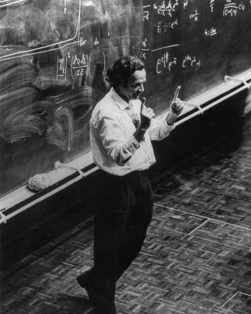 a man standing in front of a blackboard with writing on it and pointing at something