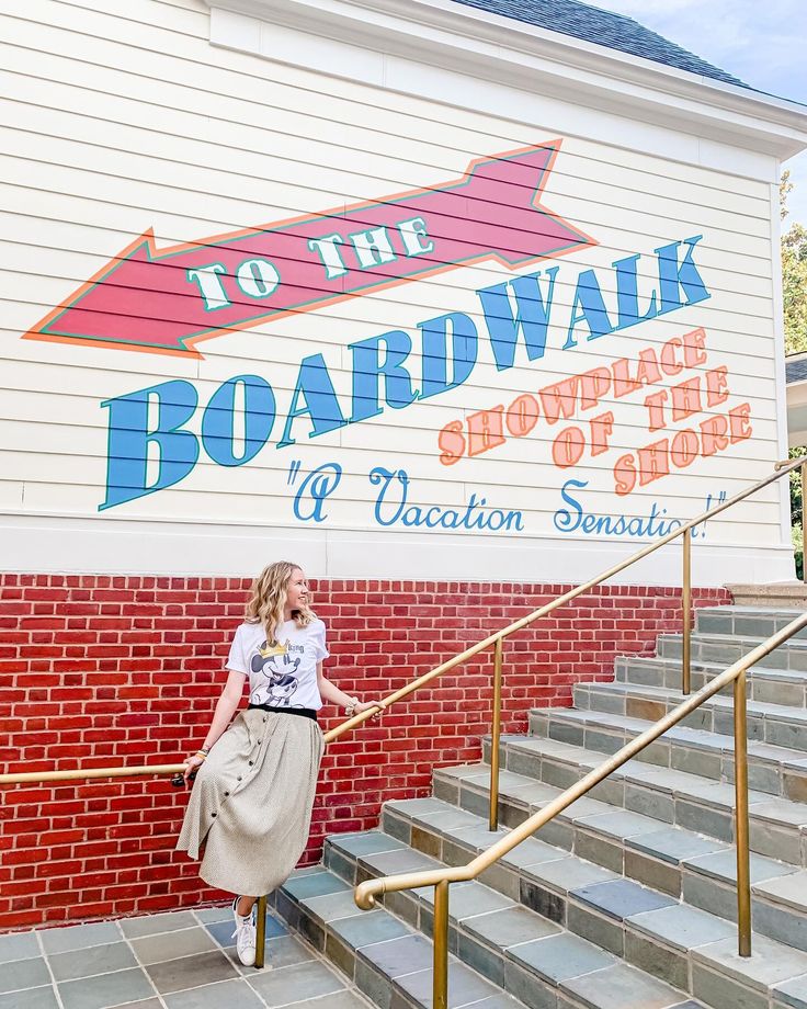 a woman standing on the stairs in front of a sign for boardwalk shopping and vacation rentals