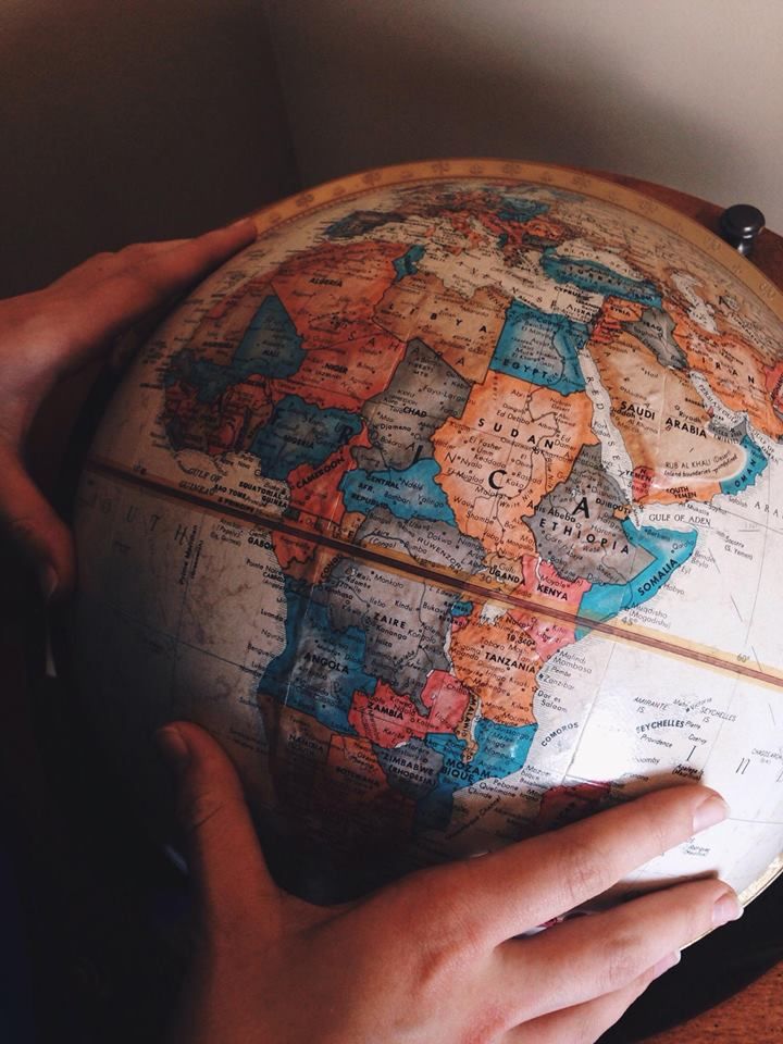 a person holding a globe in their hands on top of a wooden table next to a wall