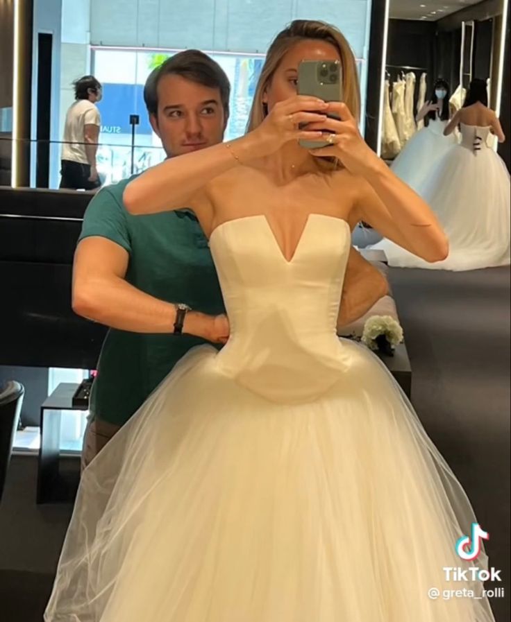 a woman in a wedding dress taking a selfie with her cell phone while standing next to a man