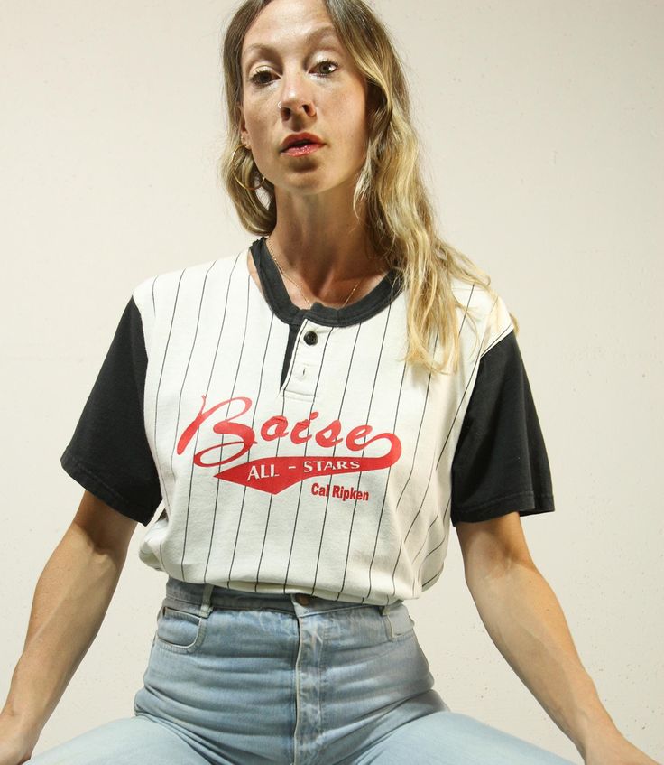 Classic Boise Baseball Tee, likely from the 90s! there is a black ringer neckline with two button closure, black short sleeves and a white Pinstripe bodice with Red writing "Boise ALL-STARS Cal Ripken" at front and "INGRAM 4" at back ~ pulls on overhead, 100% Cotton with stretch! Excellent Vintage Condition: see images for neckline re. 6" separation - patchy "4" graphic. Sold As Is. Label: Badger TM Sport. MADE IN U.S.A. M 100% COTTON Approx Best Fit: Med - XL Shoulders: 18.5" Bust: up to 40" Wa 90s Striped Short Sleeve Tops, 90s Style Black Short Sleeve Tops, Black Crew Neck T-shirt With Button Closure, Black T-shirt With Button Closure For Spring, Black Spring T-shirt With Button Closure, 90s Short Sleeve Tops With Button Closure, Spring Black T-shirt With Button Closure, Retro Black Tops With Button Closure, Black Button Closure T-shirt For Spring