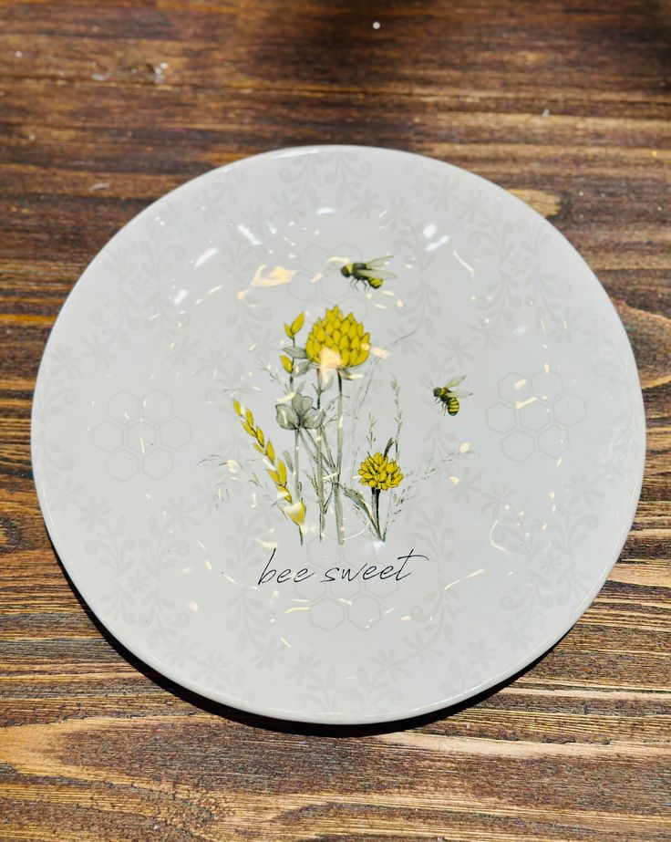 a white plate with yellow flowers and bees painted on the side, sitting on a wooden table