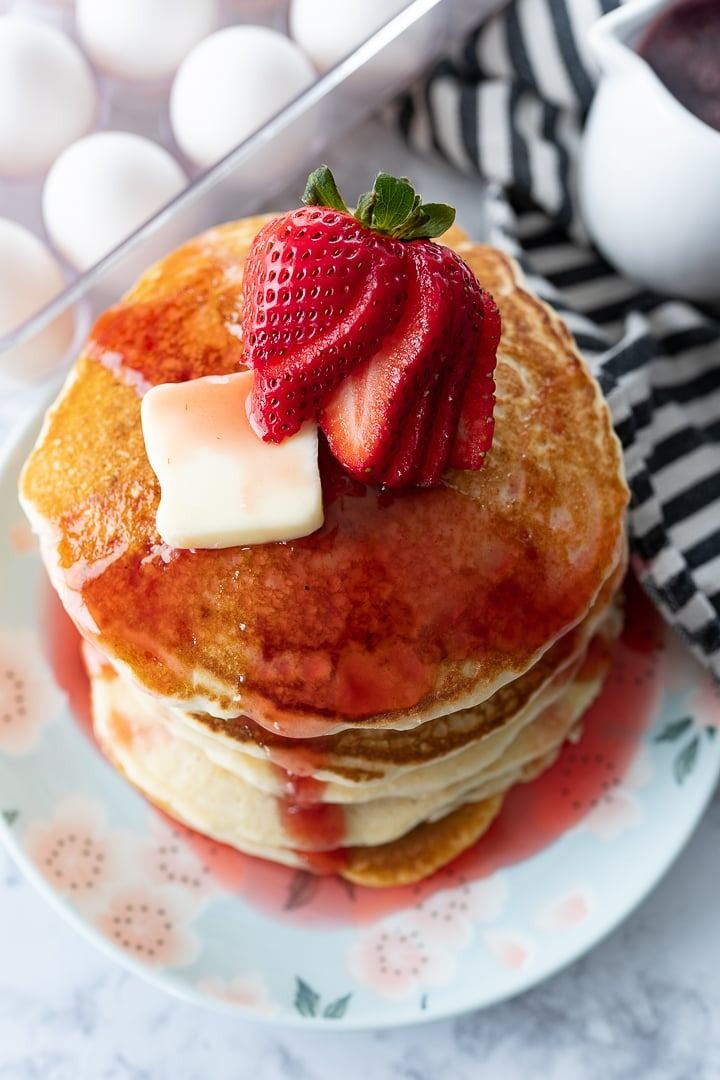 a stack of pancakes with butter and strawberries on top