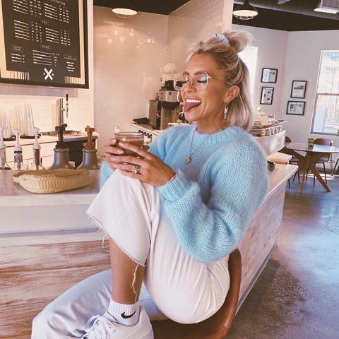 a woman sitting on a counter in a coffee shop smiling and looking at her cell phone