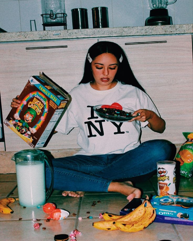 a young woman sitting on the floor holding a box of candy and eating some bananas