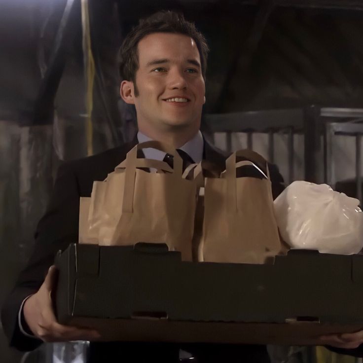 a man in a suit holding two brown paper bags with one bag on top of it