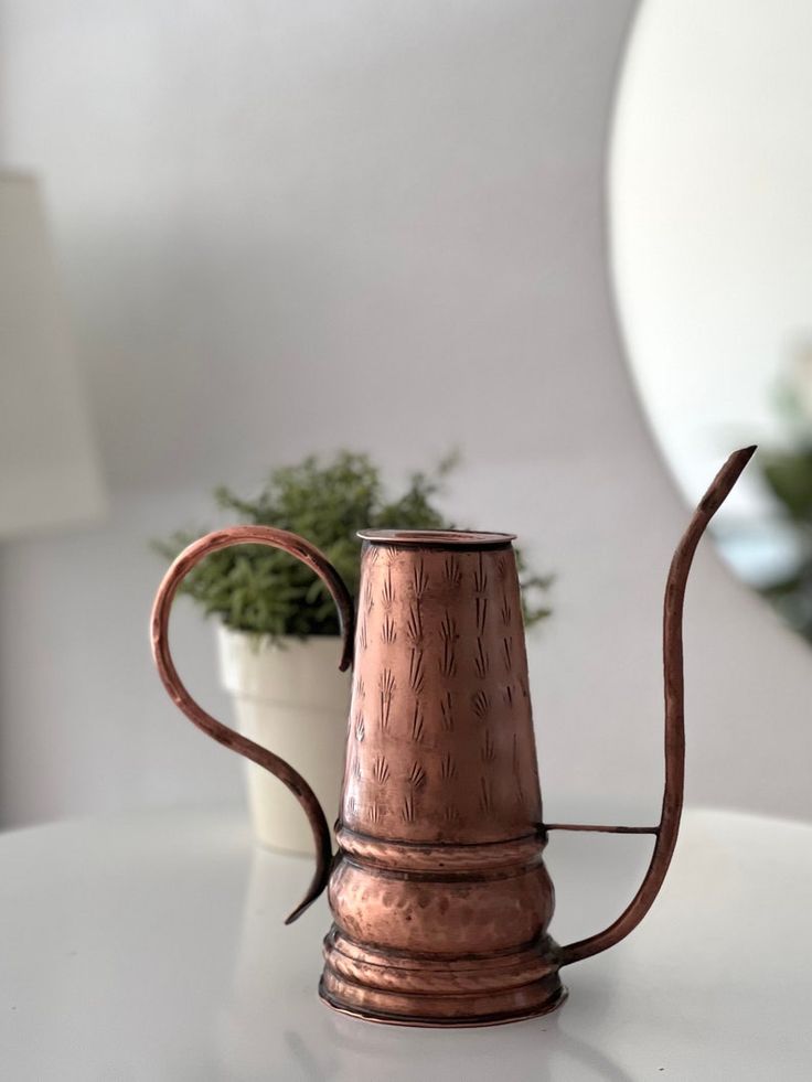 a copper coffee pot sitting on top of a table next to a white planter