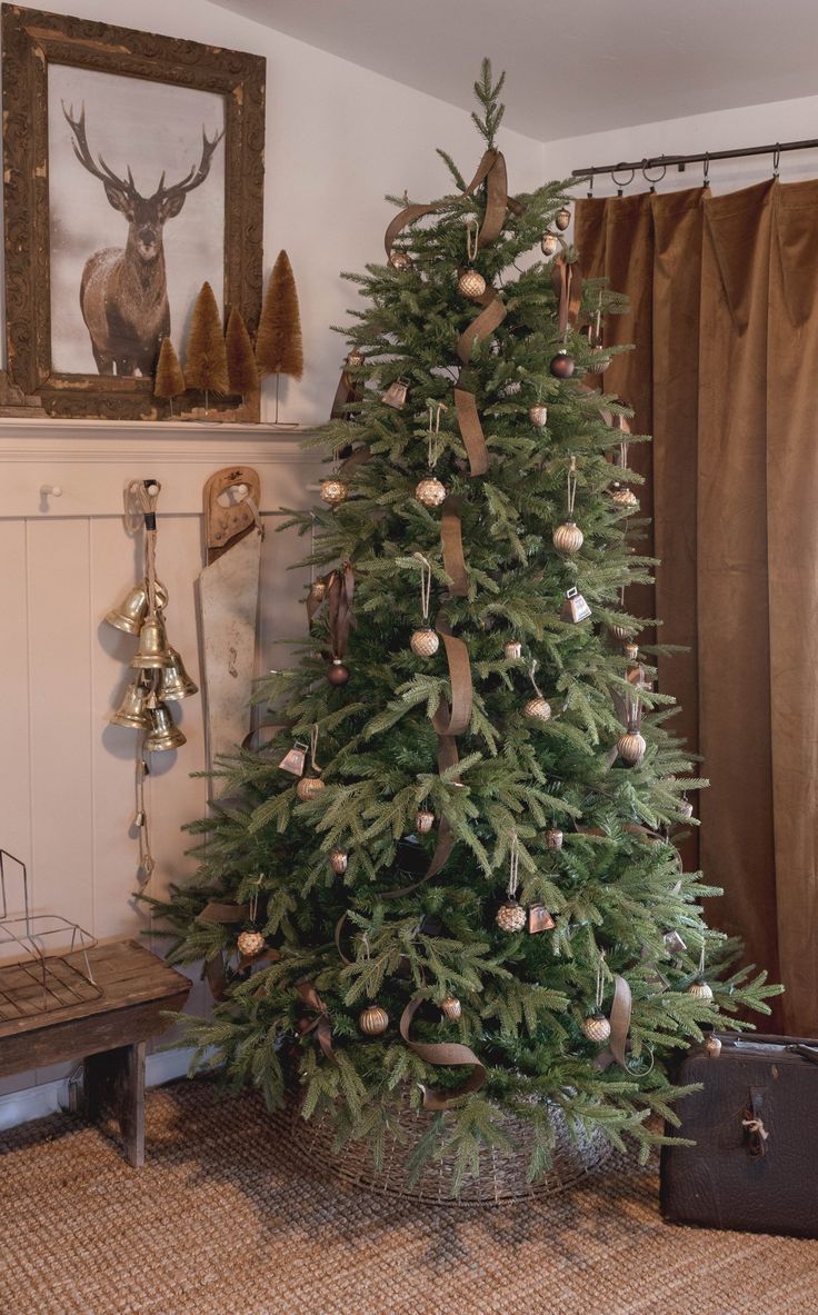 a christmas tree with ornaments on it in front of a window and a deer head