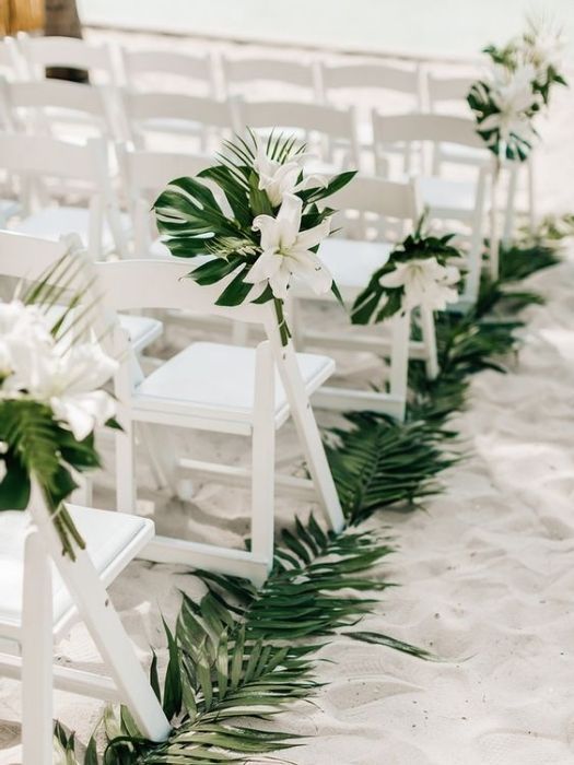 white chairs lined up on the beach with flowers and greenery in front of them