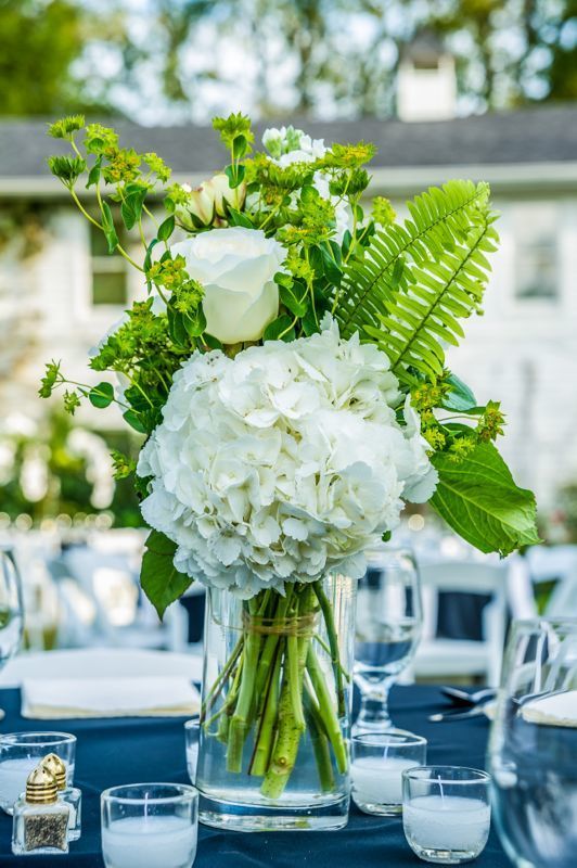 a vase filled with white flowers sitting on top of a blue table covered in glasses