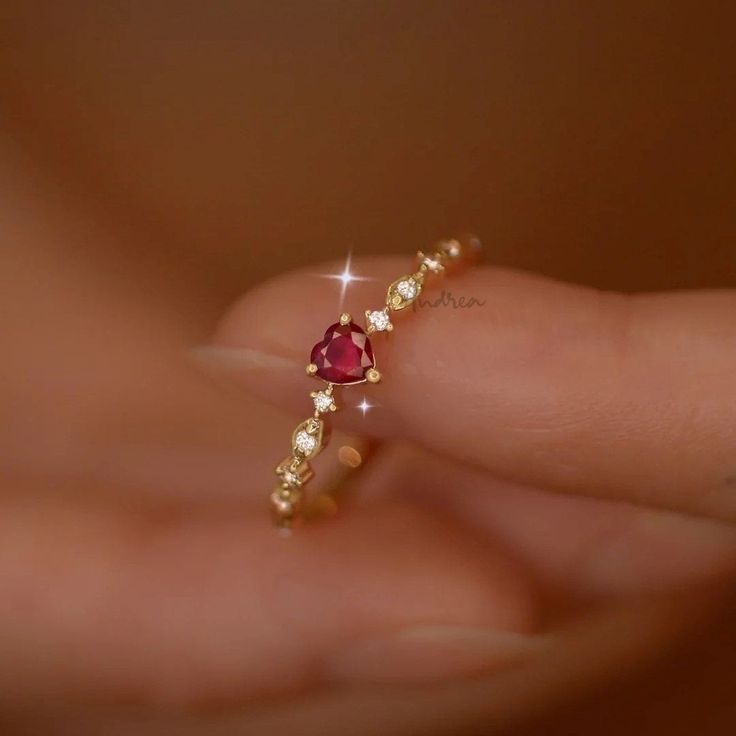 a woman's hand holding a gold ring with red and white stones