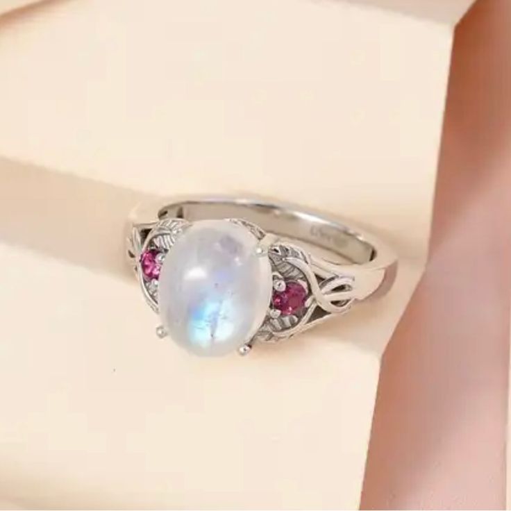 The Ring Features A Kuisa Rainbow Moonstone, Supported On Each Side By Rhodolite Garnets. These Gemstones Are Set In Platinum Over Sterling Silver. Size 6, 3.25 Ctw. New White Multi-stone Moonstone Ring, White Crystal Birthstone Ring With Round Stone, Oval White Ruby Gemstone Ring, White Multi-stone Moonstone Promise Ring, White Moonstone Ring With Gemstone Accents, White Ruby Ring Gift, White Birthstone Ring With Round Gemstone, White Birthstone Ring With Gemstone, Moonstone Multi-stone Opal Ring As Gift