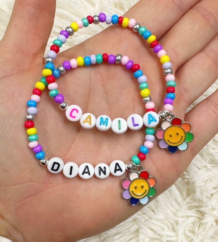 a hand holding two bracelets with name charms on each bead and an embellished smiley face charm