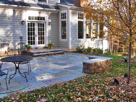 an outdoor patio with table and chairs in front of a gray house surrounded by fall leaves