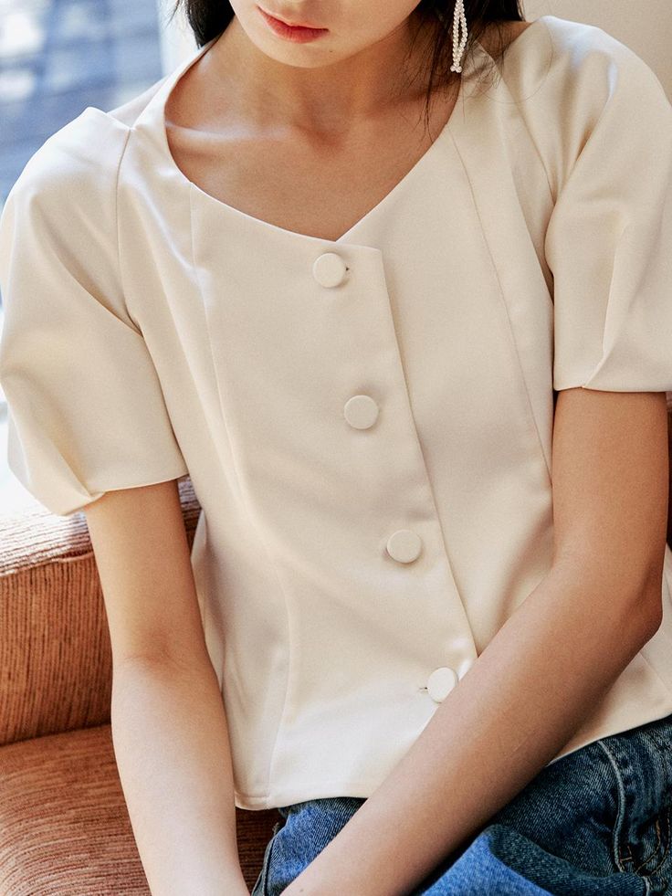 This top showcases a dramatic square neckline with a distinctive tie detail at the back, adding a playful and feminine element to its design. The fitted bodice is accented with button closures down the front, enhancing its tailored appearance. Puff sleeves contribute to the top's vintage-inspired charm, while the silhouette maintains a modern edge. The fabric appears smooth, suggesting a blend of comfort and formality suitable for various settings.- The square neckline and tie detail create an eye-catching back view.- Puff sleeves are a romantic nod to retro styles, yet remain on-trend.- Its fitted shape and button front give the top a polished look that could transition from daywear to evening wear. Fitted V-neck Blouse With Buttons, Elegant Fitted Tops With Covered Buttons, Fitted Summer Blouse With Button Back, Summer Fitted Blouse With Button Back, Square Neck Top With Buttons For Summer, Summer Square Neck Top With Buttons, Elegant Summer Top With Button Back, Elegant Summer Tops With Button Back, Elegant Puff Sleeve Button-up Top