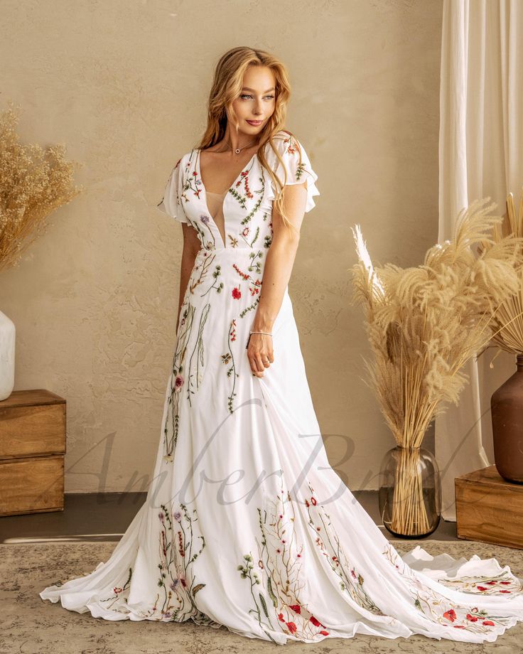 a woman in a long white dress standing next to a vase with flowers on it