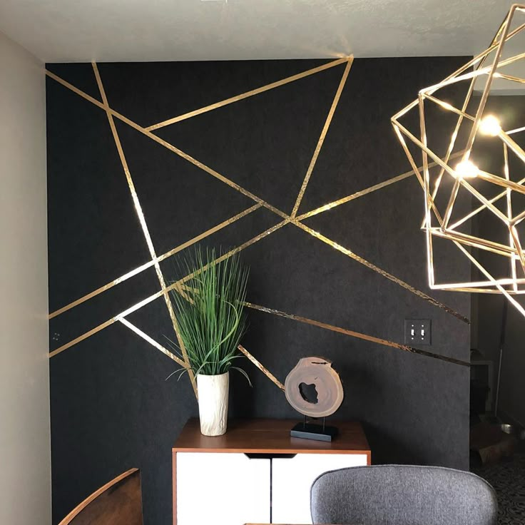 a black wall with gold lines on it and a plant in a vase next to the table