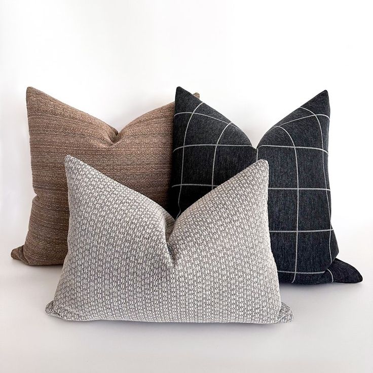 three pillows sitting side by side on top of a white surface, one black and one brown