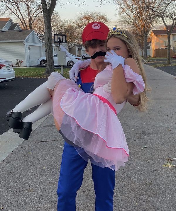 two people dressed up as mario and princess peach, one is holding an infant in her arms