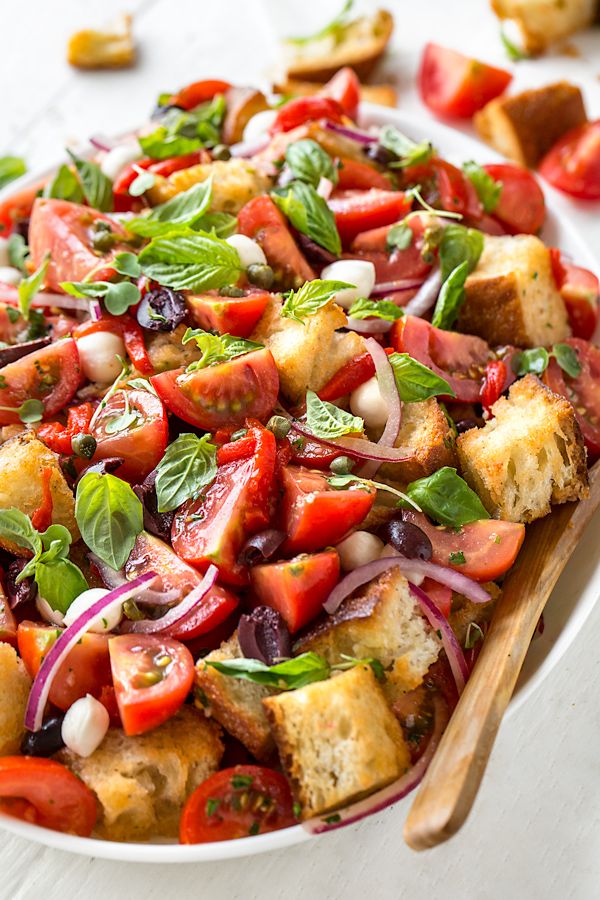 a salad with tomatoes, onions and basil in a white bowl on a wooden table