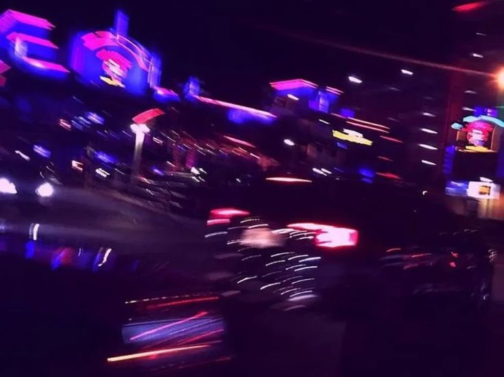 blurry photograph of neon lights and signs at an amusement park in the night time