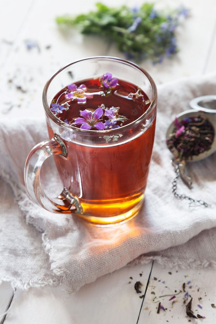 a glass mug filled with tea and flowers on top of a white cloth next to a spoon