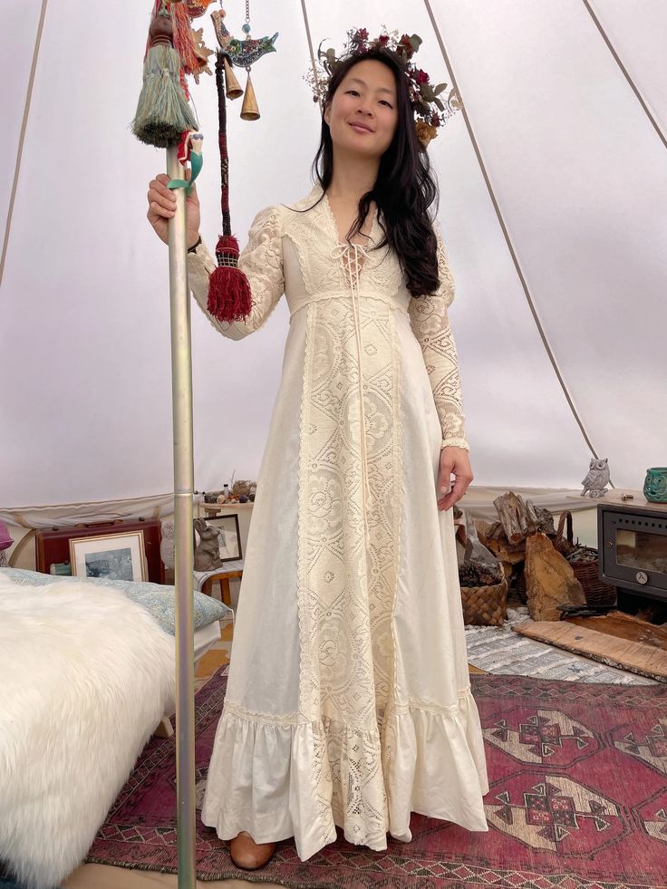 a woman in a white dress standing next to a pole with bells on top of it