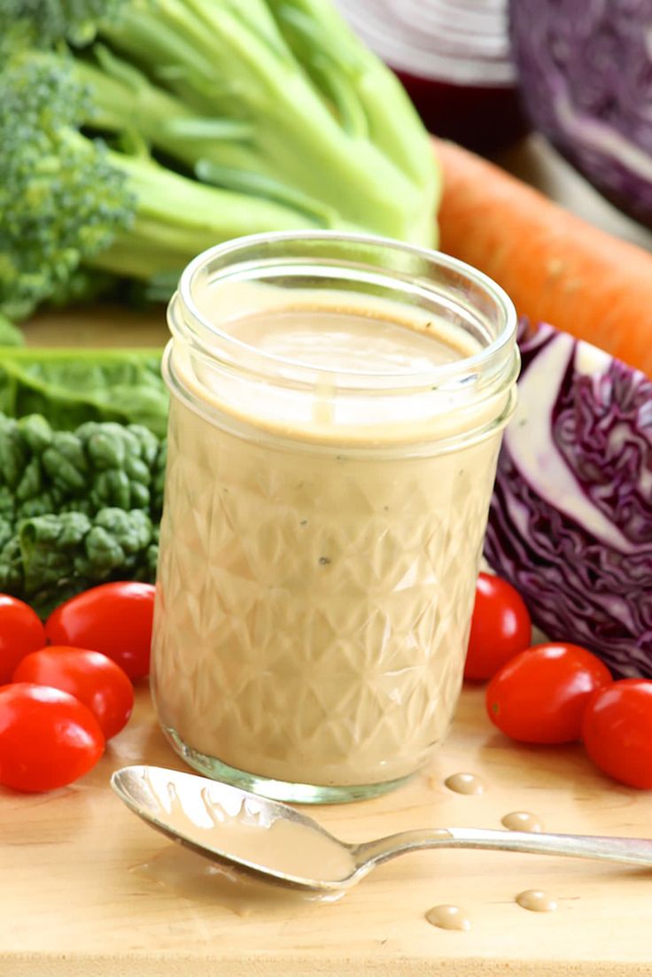 a jar filled with dressing surrounded by vegetables