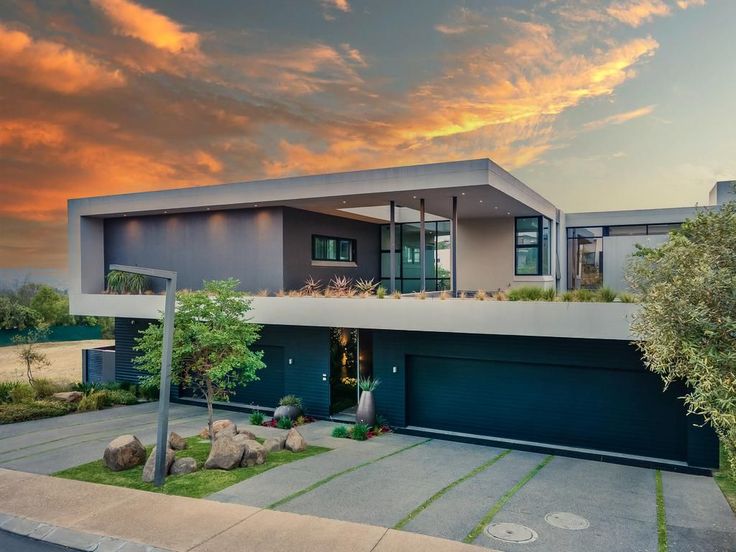 a modern house with green grass and rocks in the front yard at sunset or dawn