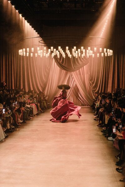 a woman in a red dress and sombrero walks down the runway at a fashion show