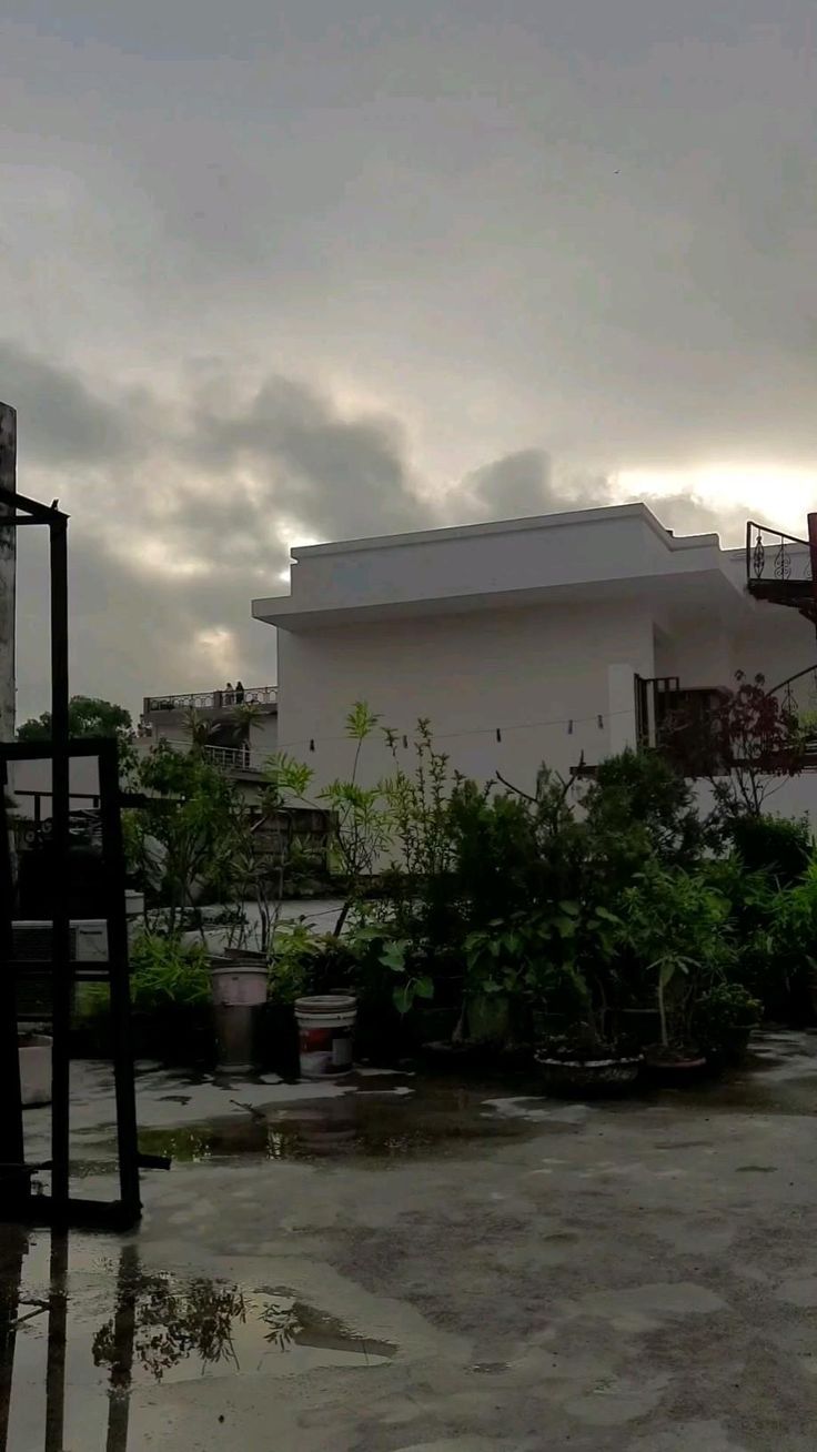 an empty parking lot in front of a white building with lots of trees and bushes