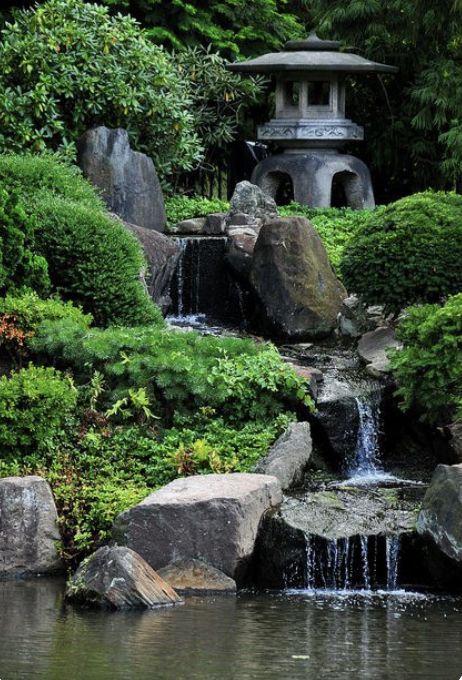 a small pond surrounded by rocks and water features a pagoda in the background with trees around it