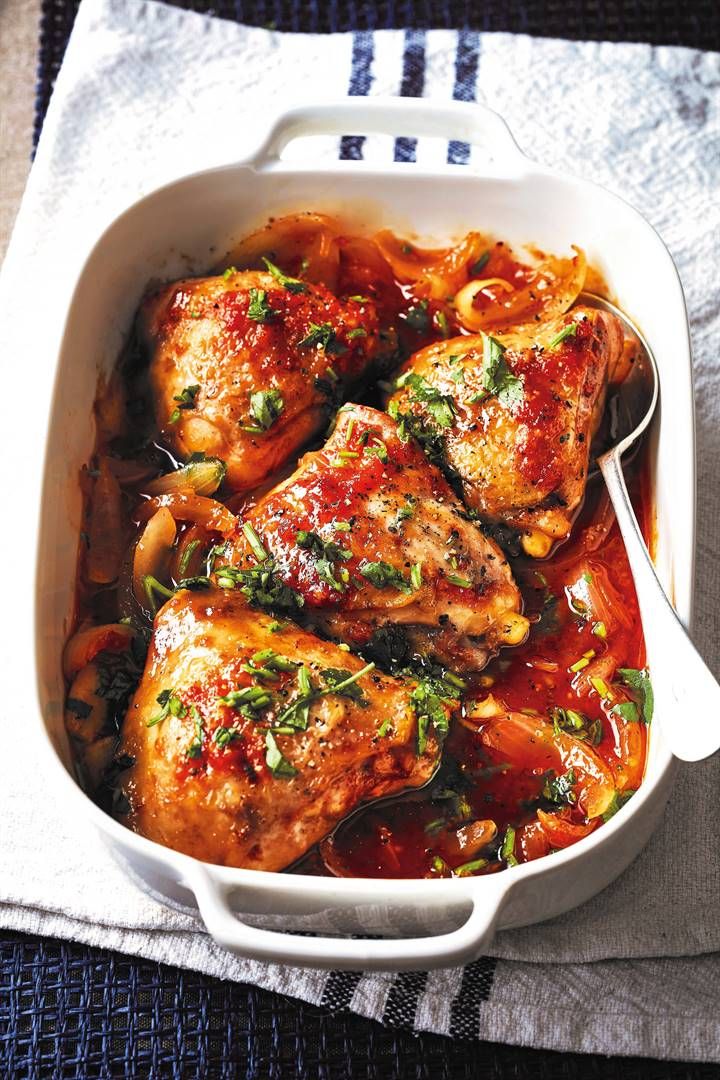 a white casserole dish filled with meat covered in tomato sauce and garnished with parsley