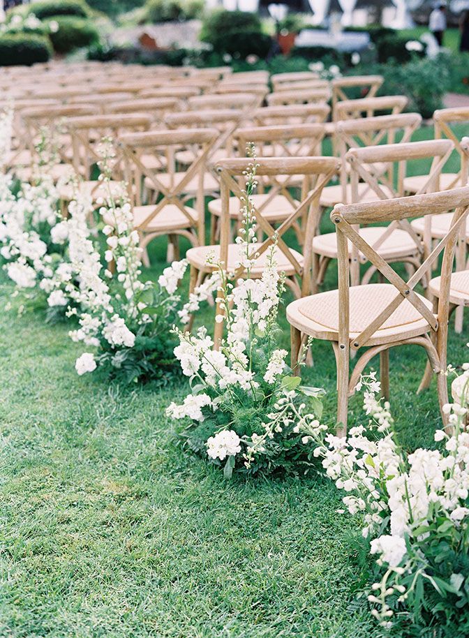 rows of chairs lined up in the grass with white flowers on each chair and one row of them