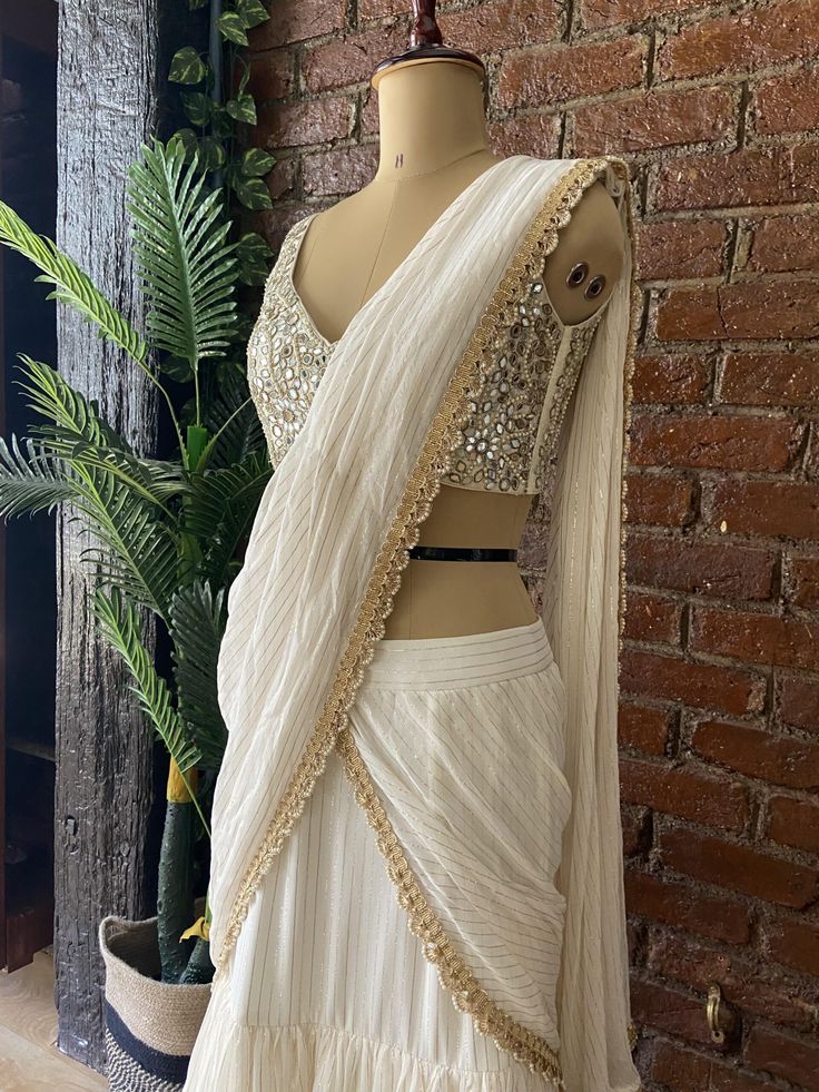 Ivory georgette pre-stitched ruffle saree with golden detailing, paired with Ivory raw silk blouse in signature Mirror and Pearl hand embroidered blouse Elegant Pre-draped Saree With Gota Work, Off White Pre-draped Saree With Cutdana, White Blouse With Sheer Dupatta For Diwali, White Georgette Pre-draped Saree For Reception, Traditional Pre-draped Off White Saree With Sheer Dupatta, Off White Pre-draped Saree With Sheer Dupatta, Designer Pre-draped Off White Saree With Sheer Dupatta, Elegant Chinon Blouse With Gota Work, White Georgette Blouse For Reception