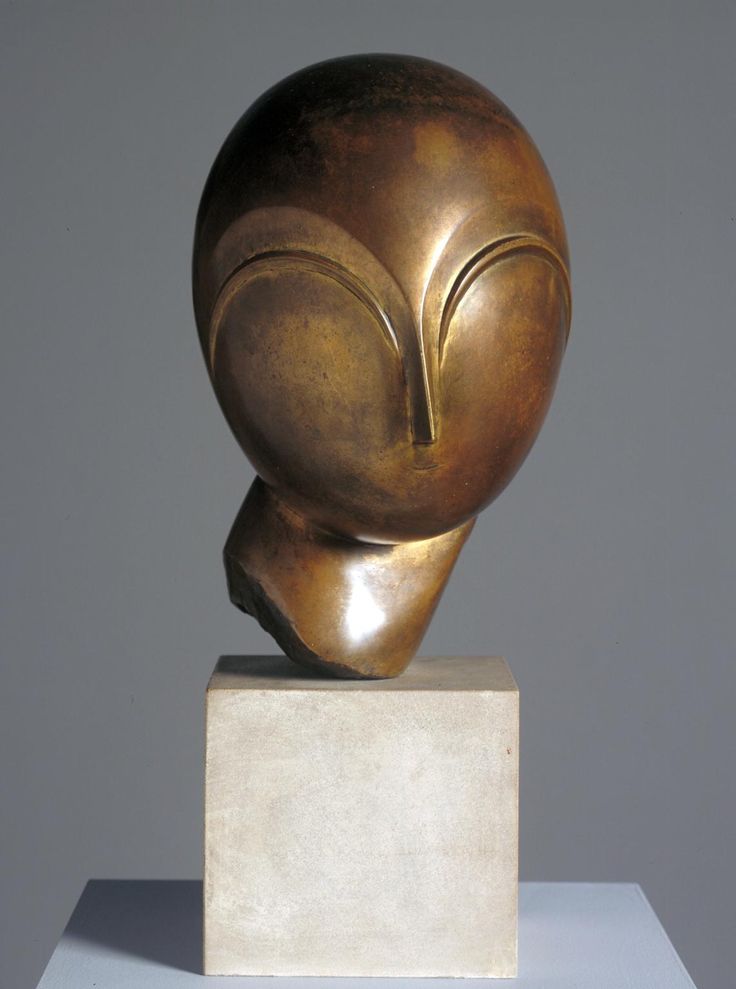 a bronze sculpture sitting on top of a white block in front of a gray wall