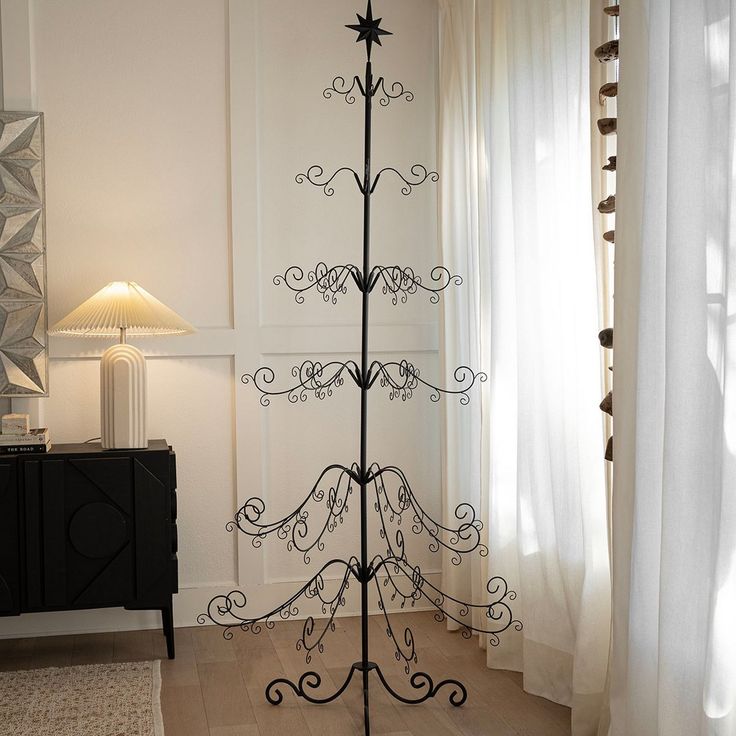 a wrought iron christmas tree stands in the corner of a room next to a window