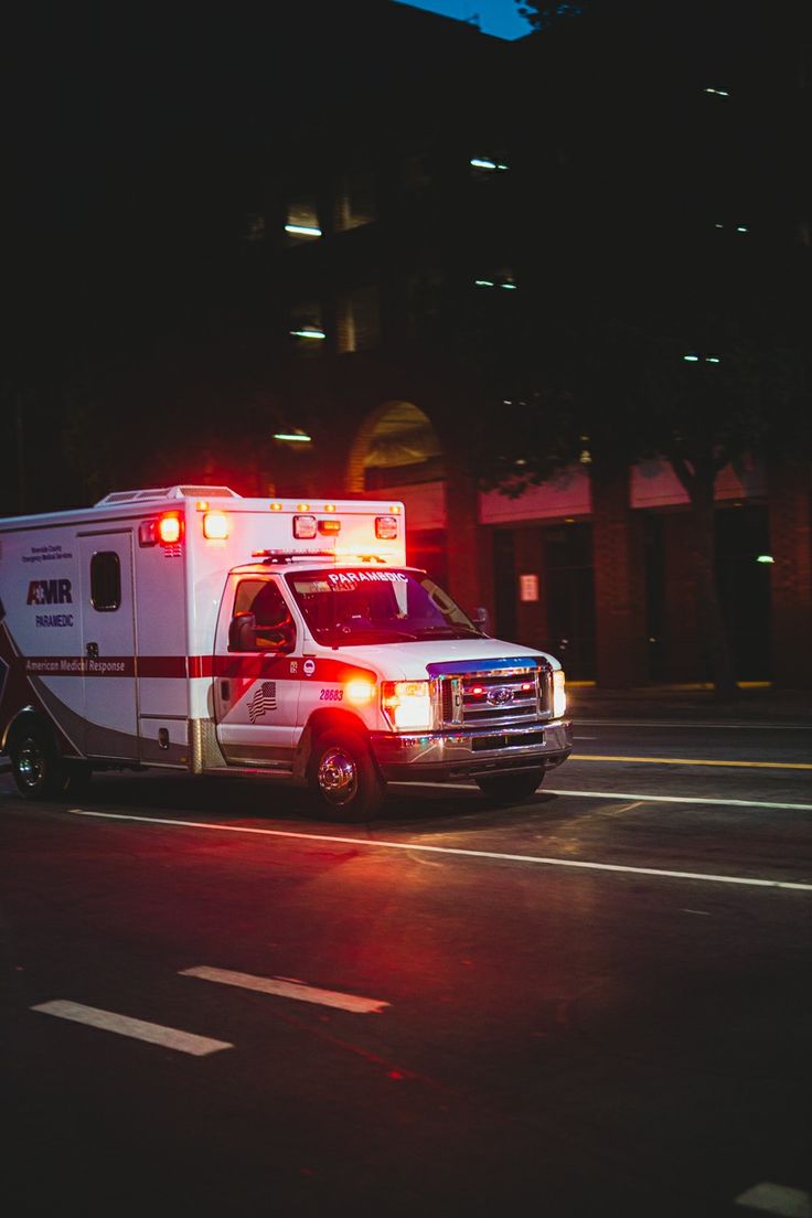 an ambulance is parked on the side of the road at night with its lights on