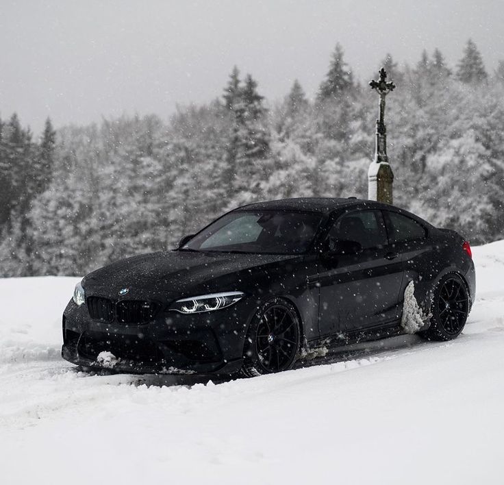 a black car driving down a snow covered road next to a cross on top of a hill