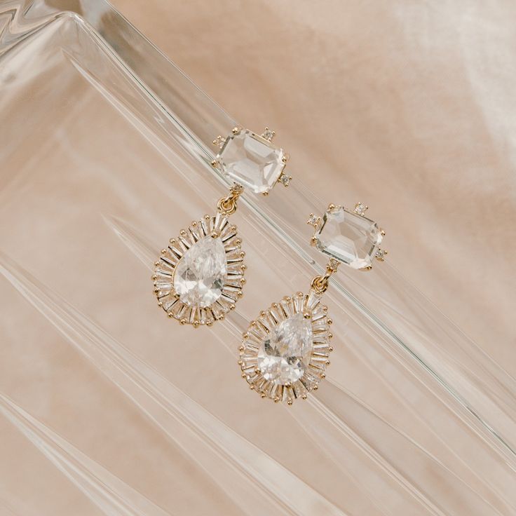 Our Clara Drop Earrings are for the classic bride, who wants a touch of art deco glam. What do we love about them? They sparkle beautifully and will not overpower your entire bridal look, just enhance it! FEATURES White cubic zirconia and glass pendant post Cubic zirconia teardrop pendant Ear post is .925 sterling which is perfect for sensitive ears!