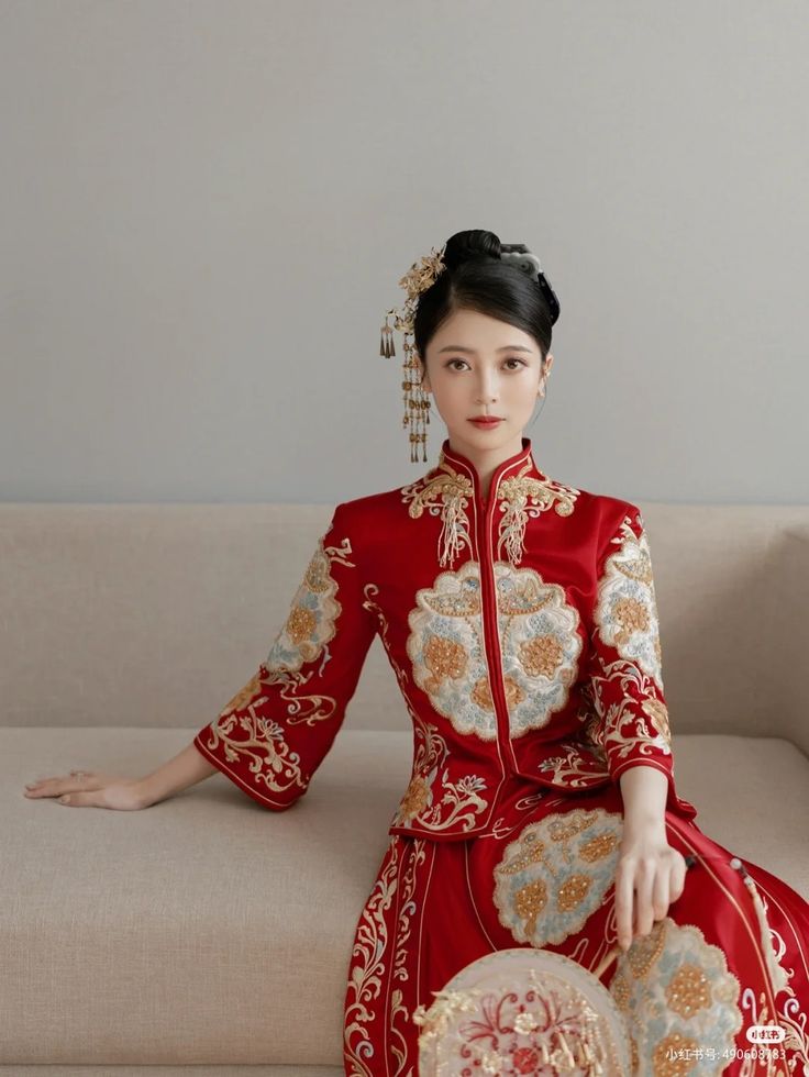 a woman sitting on top of a couch wearing a red dress and holding a fan