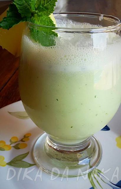 a glass filled with green liquid on top of a white and blue table cloth next to a plate