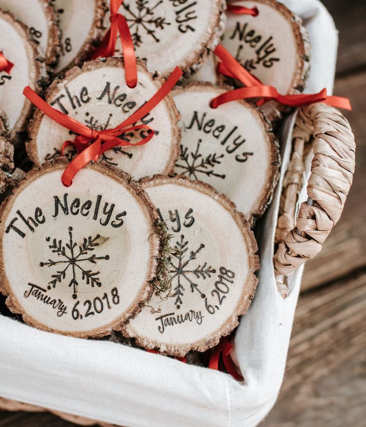 wooden slices with names and snowflakes on them are tied to red ribbon in a basket