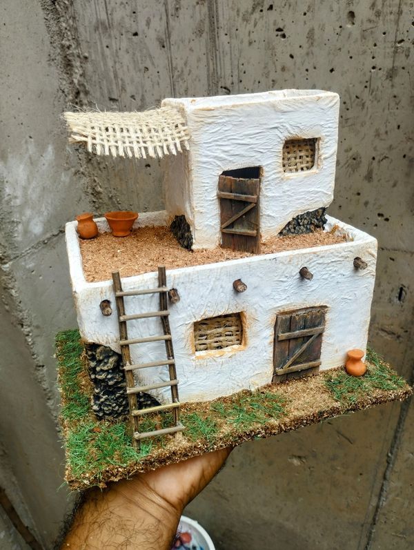 a hand holding up a fake house made out of clay and grass with windows on the roof