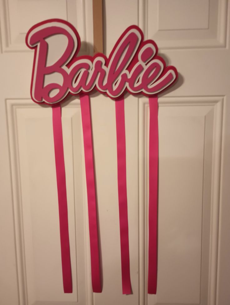 a pair of pink hair pins with the word barbie on them hanging from a door