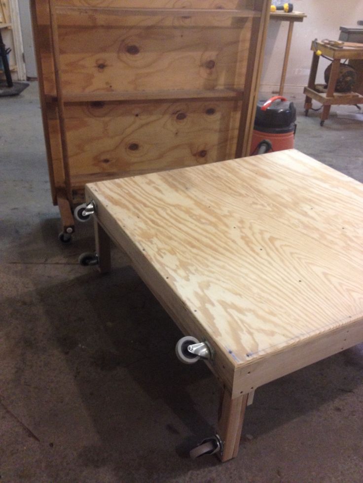 a wooden bed frame with wheels on the bottom and sides, sitting in a garage