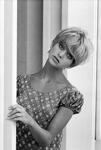 a black and white photo of a woman leaning against a wall with her hands on her hips