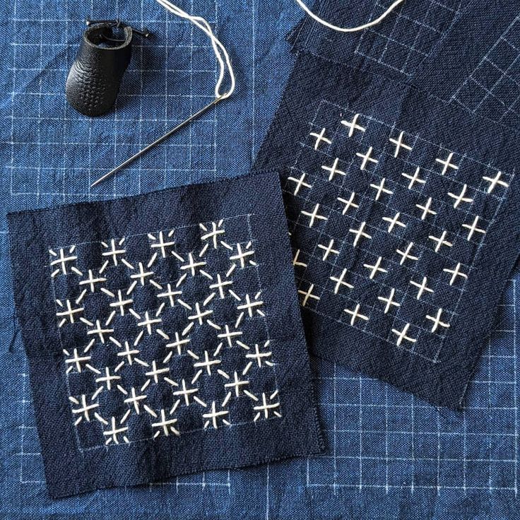 two pieces of cloth with cross stitching on them, next to a pair of scissors and thread