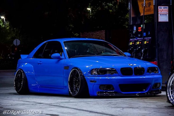 a blue car is parked in front of a gas pump at night with its lights on