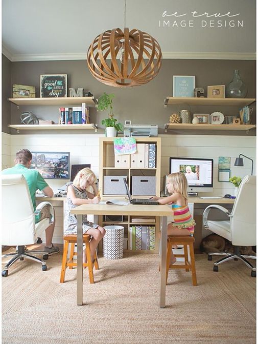 two people sitting at a desk in front of computer monitors and laptops with shelves above them